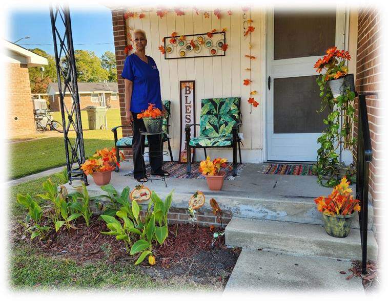 Patricial Little stands on her porch smiling and shows off her winning yard of the month.