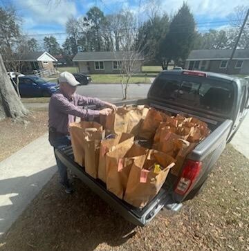 A man loading dozens of meal in paper bags in the back of a truck.