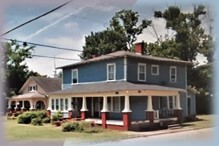 Two story blue house with a wraparound porch.