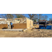 Two construction workers hard at work on the frame of a house. One is measuring and cutting wood.