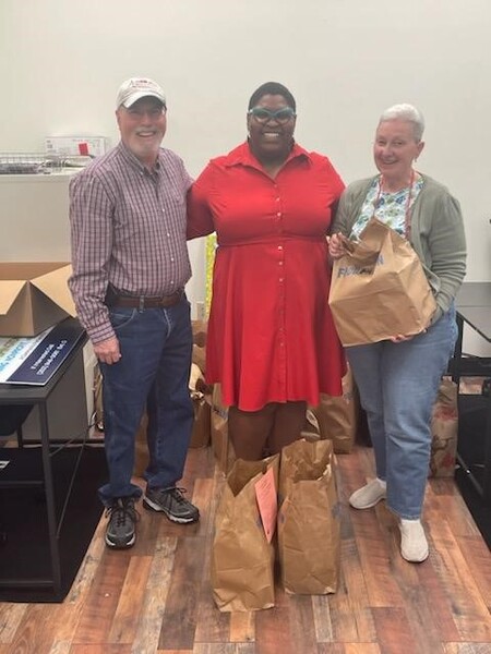 A woman smiling with a couple holding dinner bags.