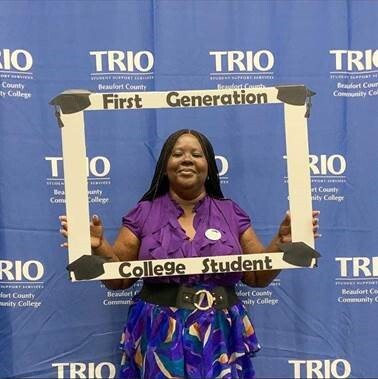 A woman holding a sign that states First Generation College Student.