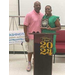 A man stands with the award recipient holding her award, behind a podium with a 2024 graduation decoration mounted on it. 