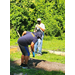 A gentleman with a hoe standing by the man with the weedeater.