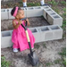 Young girl with a shovel next to a garden bed.