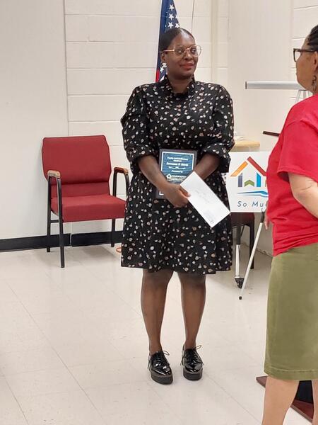 Woman standing  holding an envelope and a plaque.