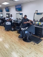 Men with aprons over them getting their hair cut by barbers. 