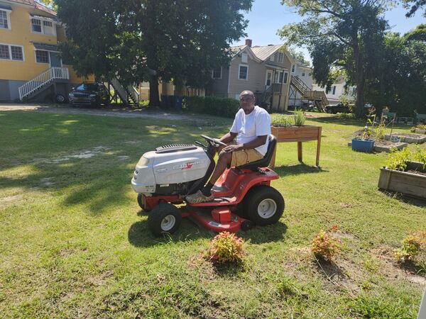 Man on a riding lawnmower in the Community Garden.