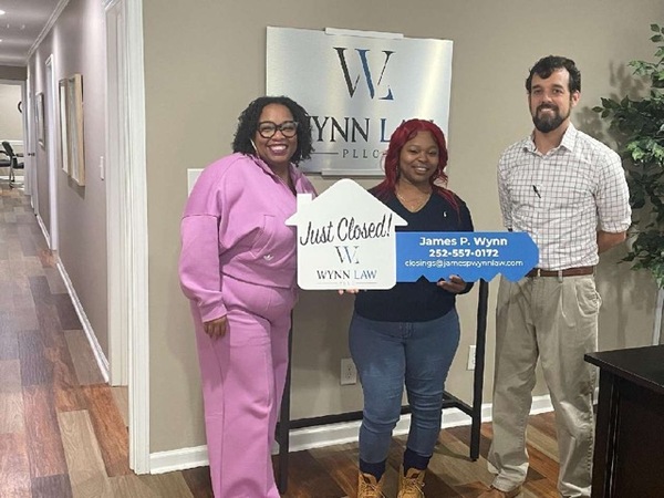 Individuals holding a for sale sign from a home.