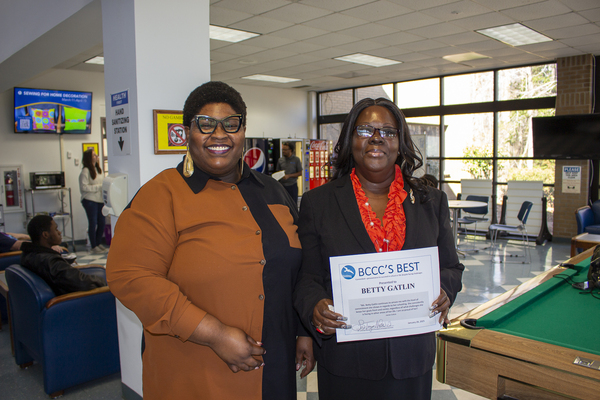 Two ladies standing next to each other in a rec room. One lady is holding a certificate.