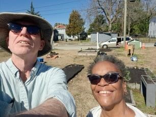 CommunityGarden2300.jpg Two people with the community garden in the background.